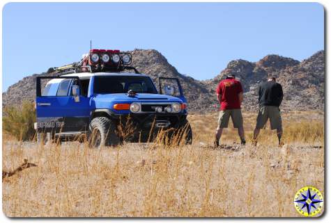 men peeing side of dirt road next to fj cruiser